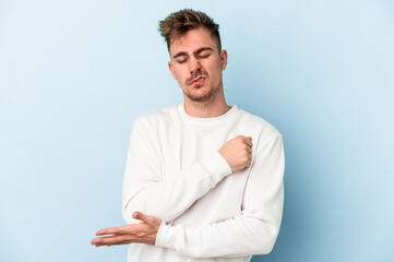 Young caucasian man isolated on blue background massaging elbow, suffering after a bad movement.