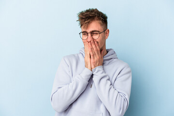 Young caucasian man isolated on blue background laughing about something, covering mouth with hands.