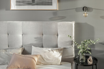 Modern bulb lamp with black metal detail on grey wall in contemporary style bedroom interior  with soft cotton in beige tones bed linen and light grey bed furniture