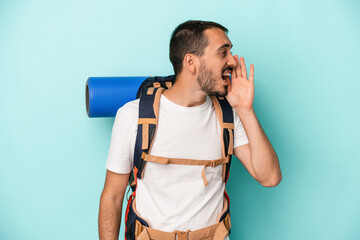 Young caucasian hiker man isolated on blue background shouting and holding palm near opened mouth.