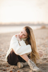 Fototapeta na wymiar Long-haired blonde girl sitting on the sandy beach in the autumn morning