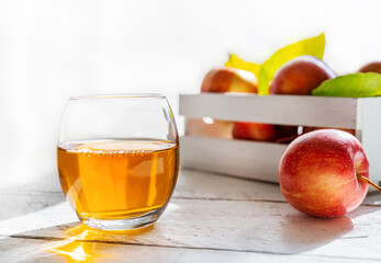 Apple juice in the glass with apples in box on white wooden table