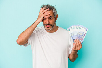 Middle age caucasian man holding bills isolated on blue background  being shocked, she has remembered important meeting.