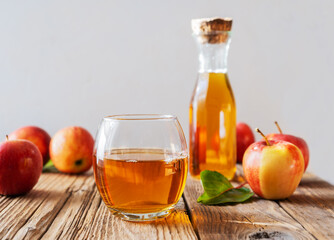 Apple juice in the glass and jar with apples, leaf on the wooden table and light grey background