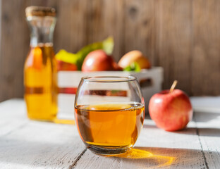 Apple juice in the glass with apples, bottle on the wooden background