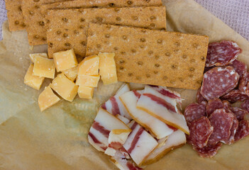 Sliced lard, sausage, ham, bacon, salami, diced cheese lay near breadcrumbs on permanent brown paper view from above. A picnic in nature. Pork or beef meat cuts top view. Dinner, lunch, branch snack.