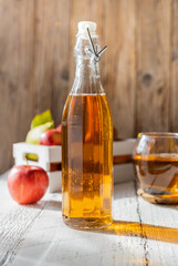 Apple juice in the glass bottle with apples in box, glass of juice on wooden background