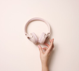 female hand hold pink wireless headphones on a beige background, top view