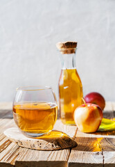 Apple juice in the glass with apples, bottle on the wooden table and light grey background