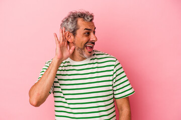 Middle age caucasian man isolated on pink background  trying to listening a gossip.