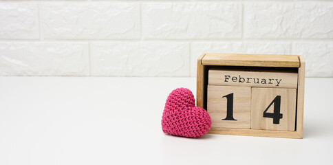 wooden calendar with date February 14 and red knitted heart, white table