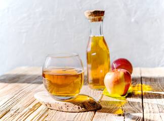 Apple juice in the glass with jar and apples on the wooden table and light grey background