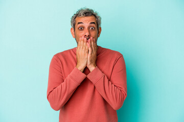 Middle age caucasian man isolated on blue background  shocked covering mouth with hands.