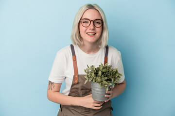 Young gardener caucasian woman holding a plant isolated on blue background laughing and having fun.
