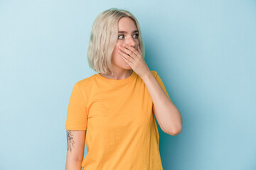 Young caucasian woman isolated on blue background thoughtful looking to a copy space covering mouth with hand.