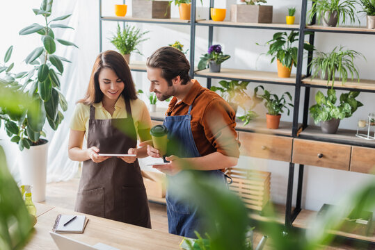 Young florists with coffee using gargets in flower shop