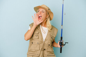 Young Russian fisherwoman isolated on blue background shouting and holding palm near opened mouth.