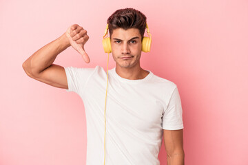 Young caucasian man listening to music isolated on pink background showing a dislike gesture,...