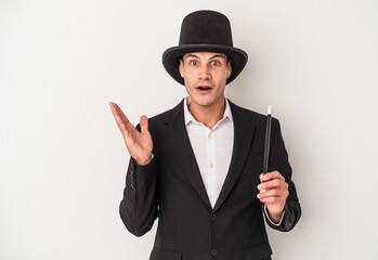 Young magician caucasian man holding a wand isolated on white background surprised and shocked.