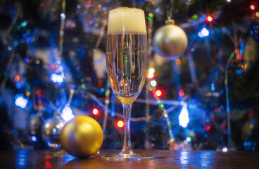 a glass of champagne and a christmas ball on the background of a christmas tree with lights