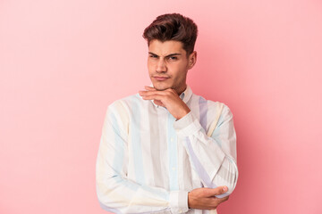 Young caucasian man isolated on pink background suspicious, uncertain, examining you.