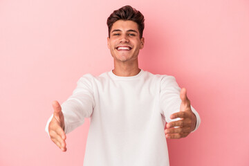 Young caucasian man isolated on pink background showing a welcome expression.