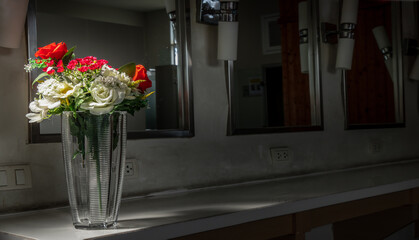 Beautiful bouquet of red and white decorative flowers in a clear glass vase on a white stone table in a dressing room. Interior design, Space for text, Selective focus.