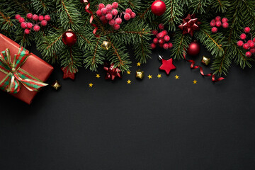 Black Christmas background with Christmas tree branches and red berries, winter festive composition with copy space. Top view.