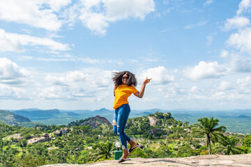 Naklejka premium a young african lady jumps with excitement, in front of a beautiful landscape