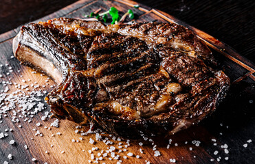 Grilled Ribeye Steak on bones on wooden board, prime cowboy steak on dark background