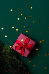 Obraz premium Red gift box with bow and sequins on a green background front view. Christmas gift flat lei