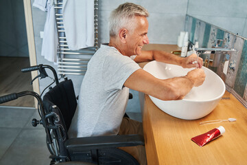Joyful wheelchair user holding hands under running water