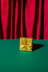 A golden gift box on a green table against the background of a red curtain. Gift on a Christmas background with space for text