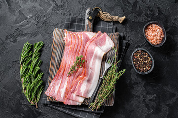 Raw smoked bacon slices with rosemary and thyme on wooden board. Black background. Top view