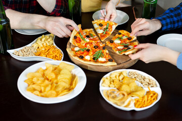 Close-up of handsome young friends drinks beer and eating pizza at pub