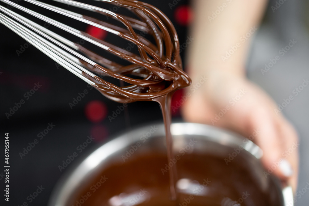 Wall mural pastry chef whips melted chocolate in a bowl with a metal wire whisk close up