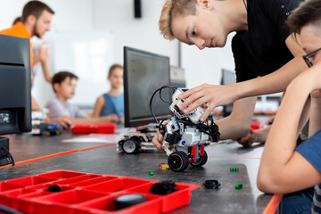 Smart schoolboy sitting at the table and constructing a robotic device in a school lesson