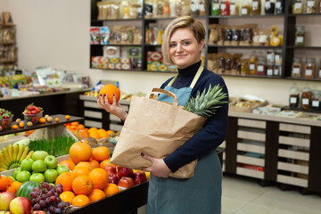 Young saleswoman collects vegetables and fruits in a paper bag.