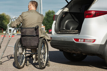 Fototapeta premium Back view of adult man using wheelchair unloading car in parking lot outdoors, copy space