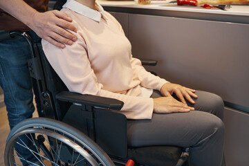 Caring man assisting woman using wheelchair in kitchen