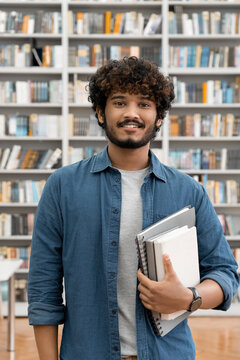 Portrait of satisfied male freelancer or student standing in university library