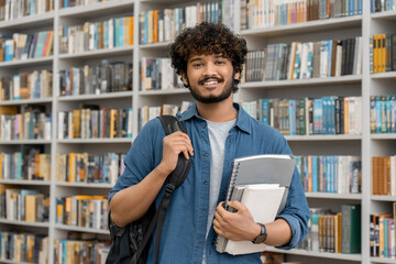 Cheerful male international student at university library or book store - obrazy, fototapety, plakaty