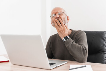 Elderly man bored and yawned while working at laptop