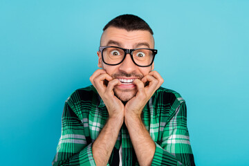 Photo of unhappy upset scared shocked young man bite fingers wear glasses horrified isolated on blue color background