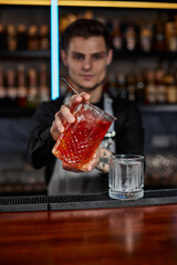 barman in apron pours old fashioned cocktail into glass