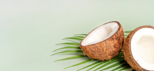 Ripe half coconut with green leaf on green background. Banner with copy space - obrazy, fototapety, plakaty