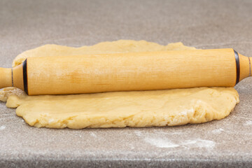 Wooden rolling pin lying on a yellow dough on a gray table sprinkled with flour. Cooking dough for pie, pizza, cookies.