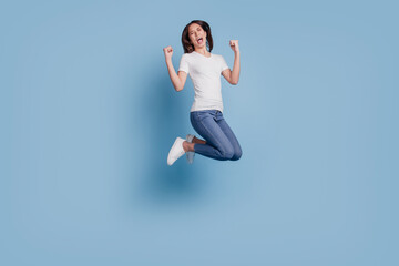 Portrait of astonished cheerful champion lady jump raise fists open mouth on blue background