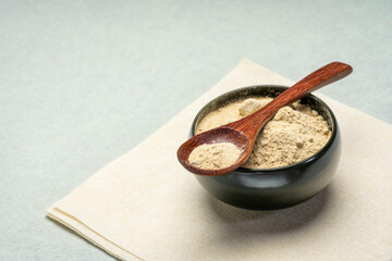 maca root powder in a small ceramic bowl with a wooden teaspoon - super food