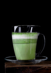 Matcha latte on plant-based milk in glass cup against the black background. Hot healthy vegan drink